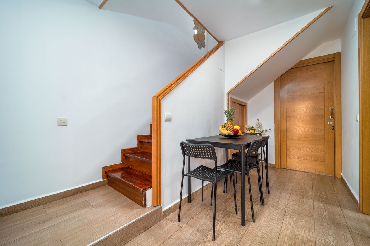Clean and minimalist interior with wooden accents, featuring a small dining area under the stairs.